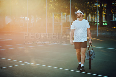 Buy stock photo Shot of a sporty young man carrying a bag while walking on a tennis court