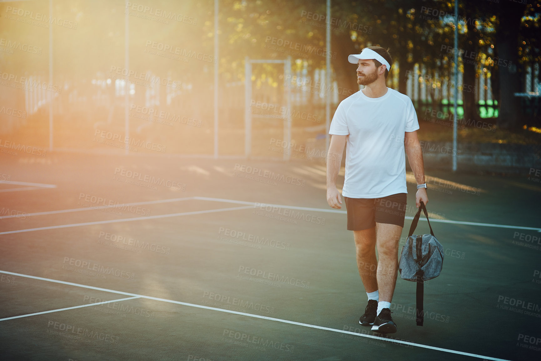 Buy stock photo Shot of a sporty young man carrying a bag while walking on a tennis court