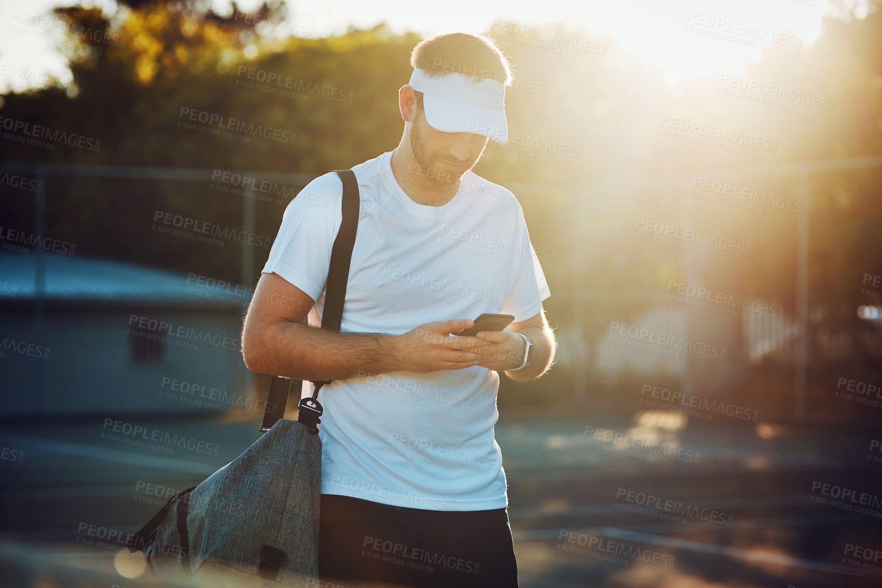 Buy stock photo Shot of a sporty young man using a cellphone while walking on a tennis court