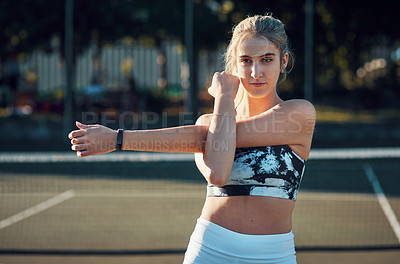 Buy stock photo Shot of a sporty young woman stretching her arms while exercising on a tennis court