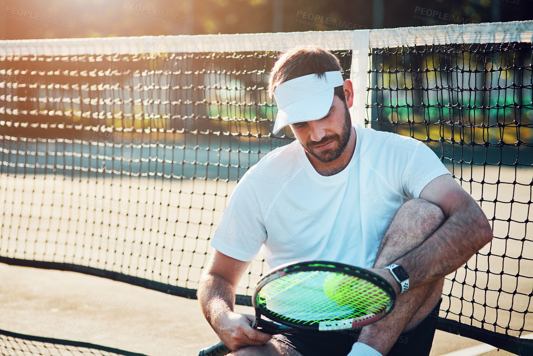 Buy stock photo Shot of a sporty young man sitting on a tennis court