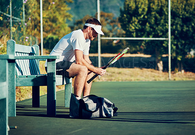 Buy stock photo Shot of a sporty young man sitting on a bench on a tennis court