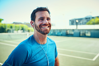 Buy stock photo Shot of a sporty young man listening to music while exercising on a tennis court