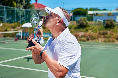 Buy stock photo Cropped shot of a handsome mature man standing and kissing his trophy after winning a tennis match during the day