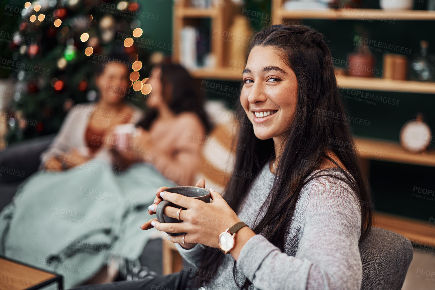 Buy stock photo Shot of a beautiful young woman enjoying a warm beverage with her friends in the background during Christmas at home