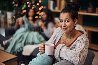 Buy stock photo Shot of a beautiful young woman enjoying a warm beverage with her friends in the background during Christmas at home