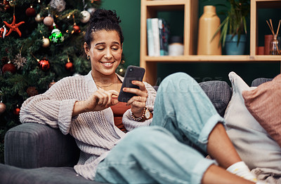 Buy stock photo Shot of a beautiful young woman using a smartphone on the sofa during Christmas at home