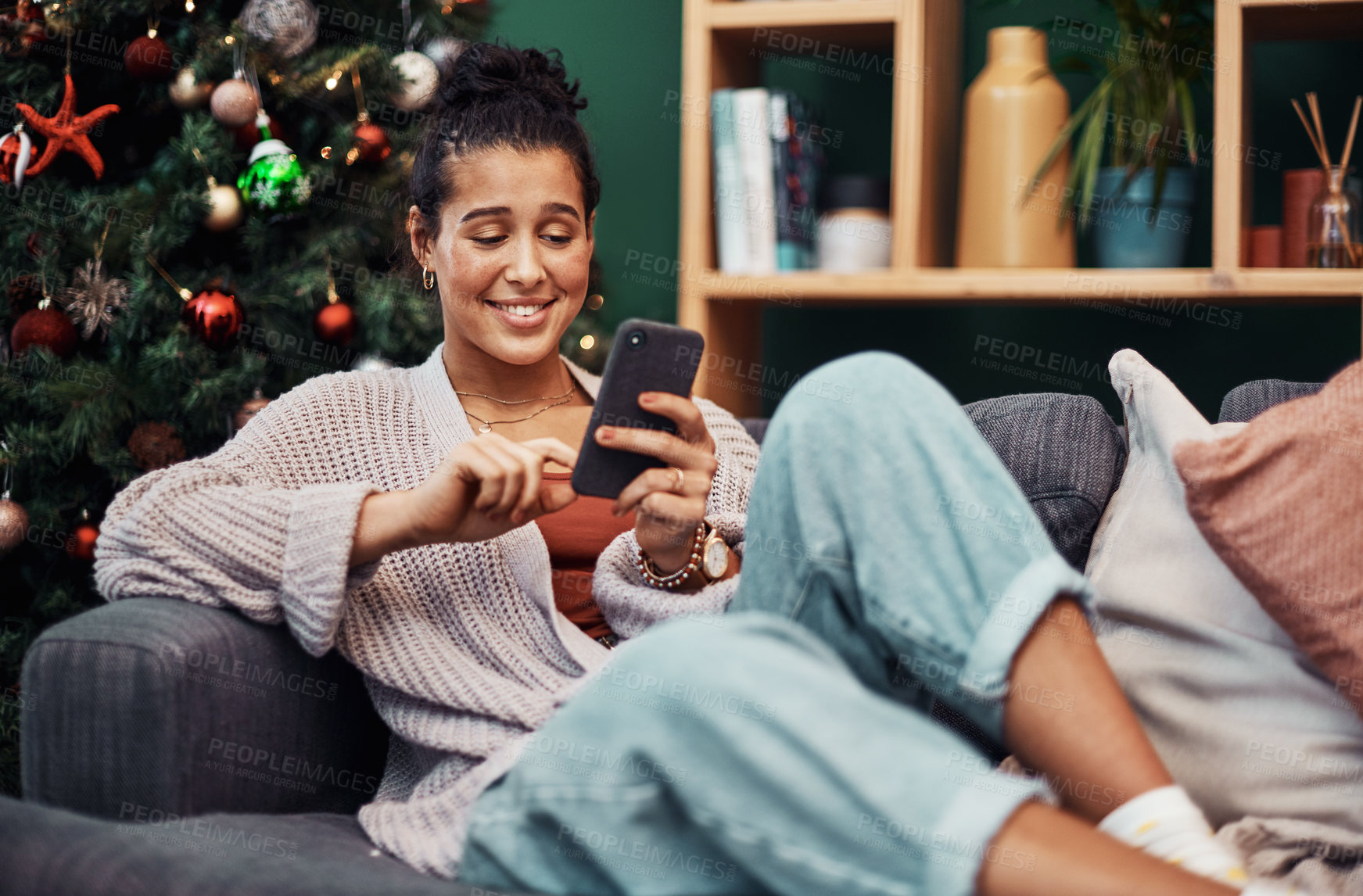 Buy stock photo Shot of a beautiful young woman using a smartphone on the sofa during Christmas at home