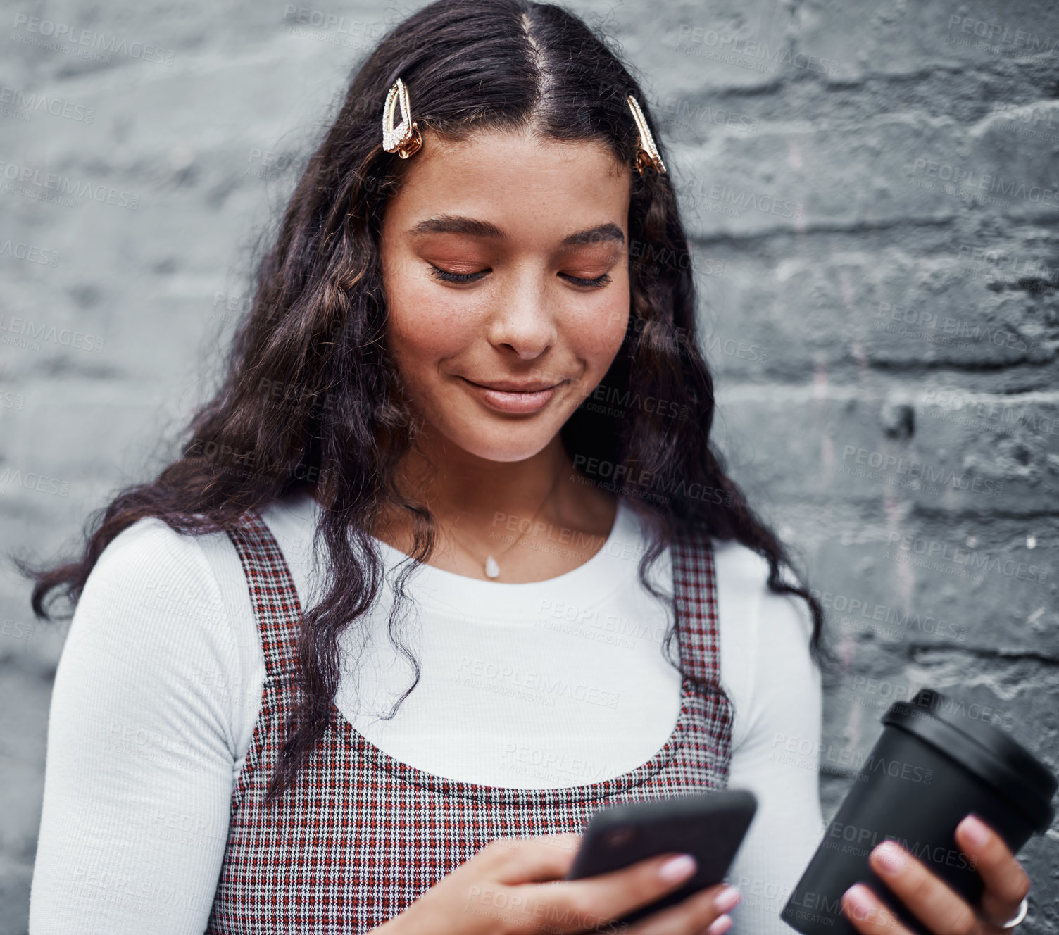 Buy stock photo Cropped shot of an attractive teenage girl standing alone and using her cellphone while holding a cup of coffee