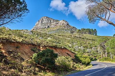 Buy stock photo Empty road in the mountains with a cloudy blue sky. Landscape of a countryside roadway for traveling on a mountain pass along a beautiful scenic nature drive with green trees and shrubs in Cape town