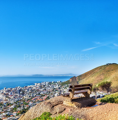 Buy stock photo Beautiful aerial view of empty bench overlooking city and ocean in Cape Town, South Africa against blue sky copyspace. A calm sunny day with a park chair on a cliff, with scenic views and fresh air 