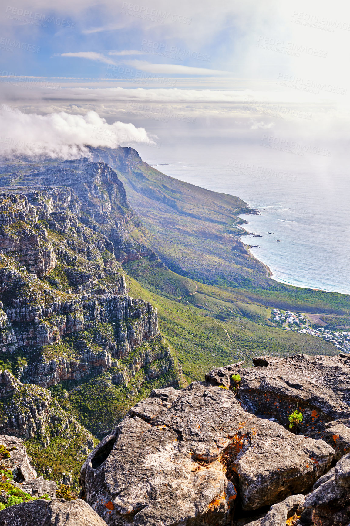 Buy stock photo High angle of a mountain coastline with a cloudy sky in South Africa. Scenic landscape of soft white clouds covering Table Mountain near a calm peaceful sea in Cape Town with sun flare and copy space
