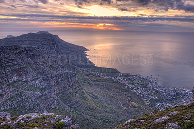Buy stock photo Aerial view of mountains by the ocean and a cloudy sunset sky copy space. Beautiful landscape of rocky green mountains top surrounding an urban city and a calm sea in Cape Town, South Africa