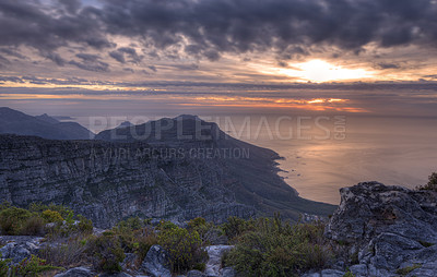 Buy stock photo Above view of a mountain coastline at sunset in South Africa. Scenic landscape of dark clouds over a calm and peaceful ocean near Cape Town with the sun behind grey clouds in the sky and copy space