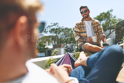 Buy stock photo Over the shoulder shot of a cheerful young man hanging out with his friend outside on their balcony at home