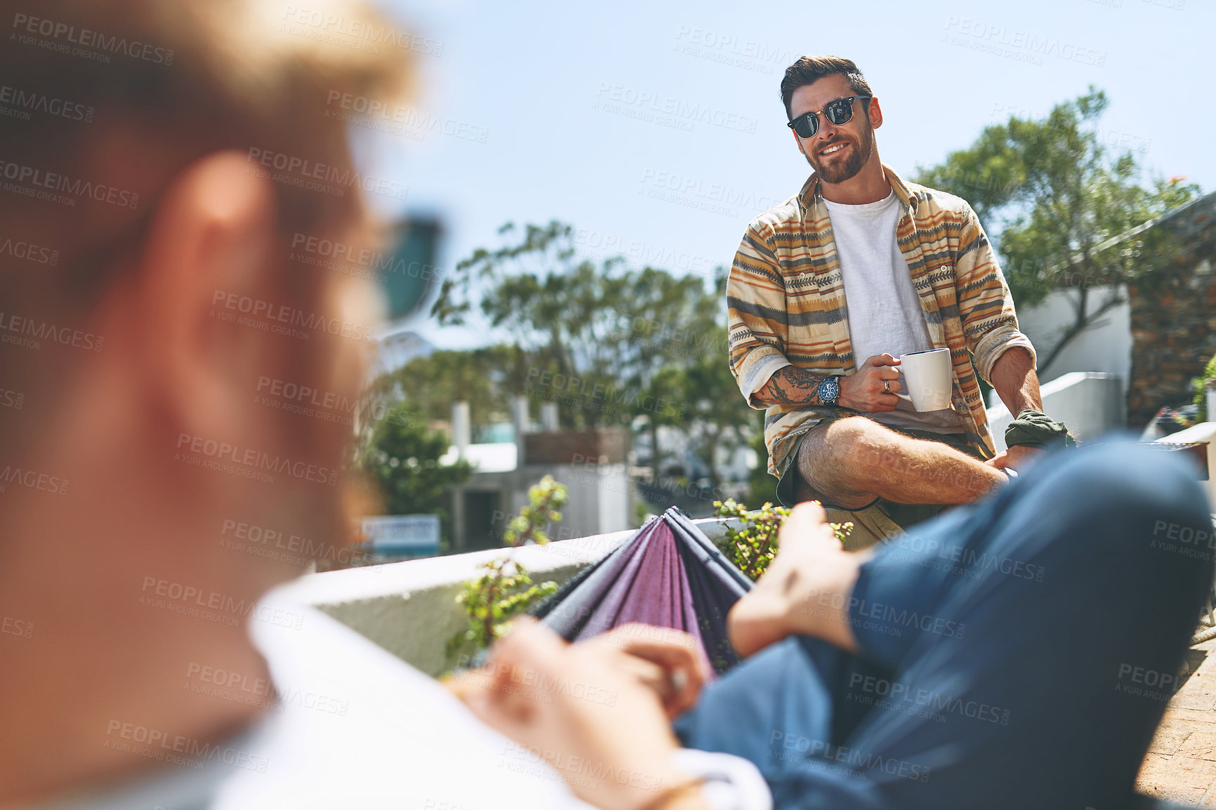 Buy stock photo Over the shoulder shot of a cheerful young man hanging out with his friend outside on their balcony at home