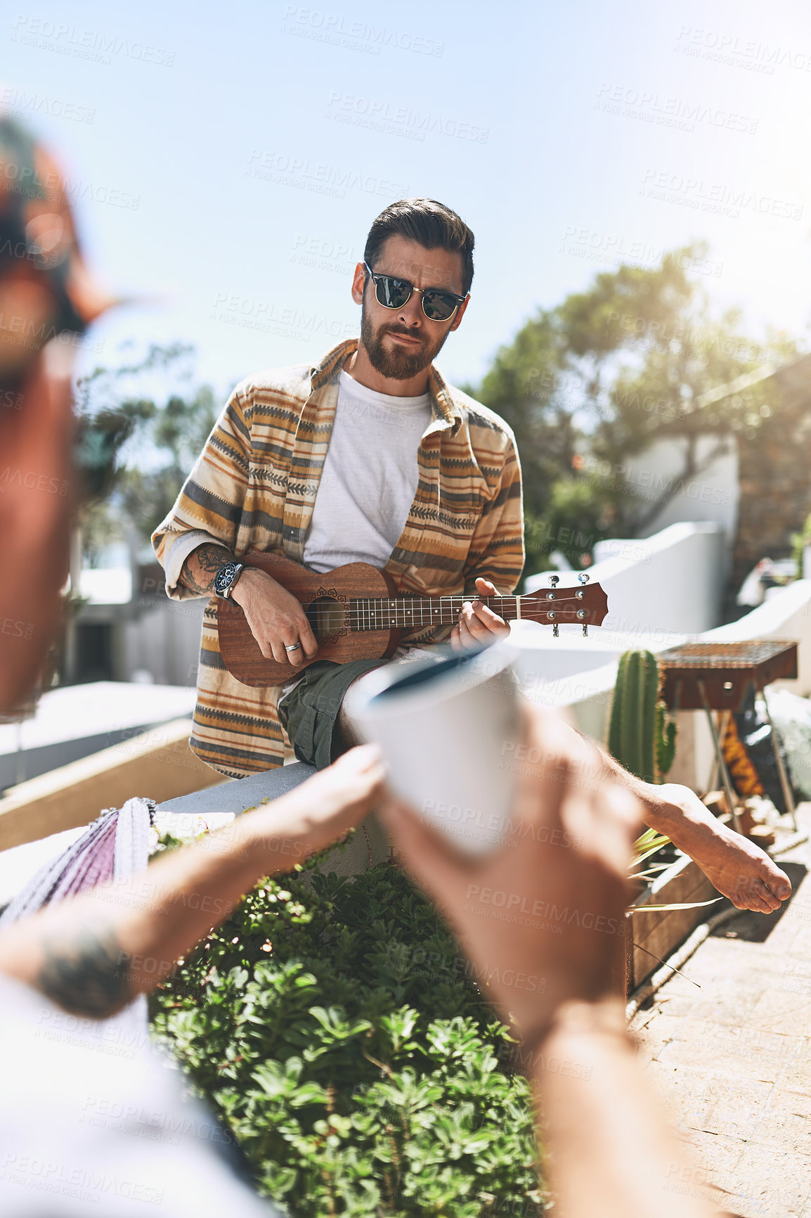 Buy stock photo Cropped shot of a cheerful young man playing on his guitar while his friend listens outside on a balcony during the day