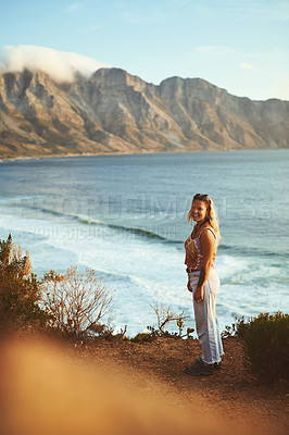 Buy stock photo Full length shot of an attractive young woman standing alone on a mountainside near the sea during a day outdoors