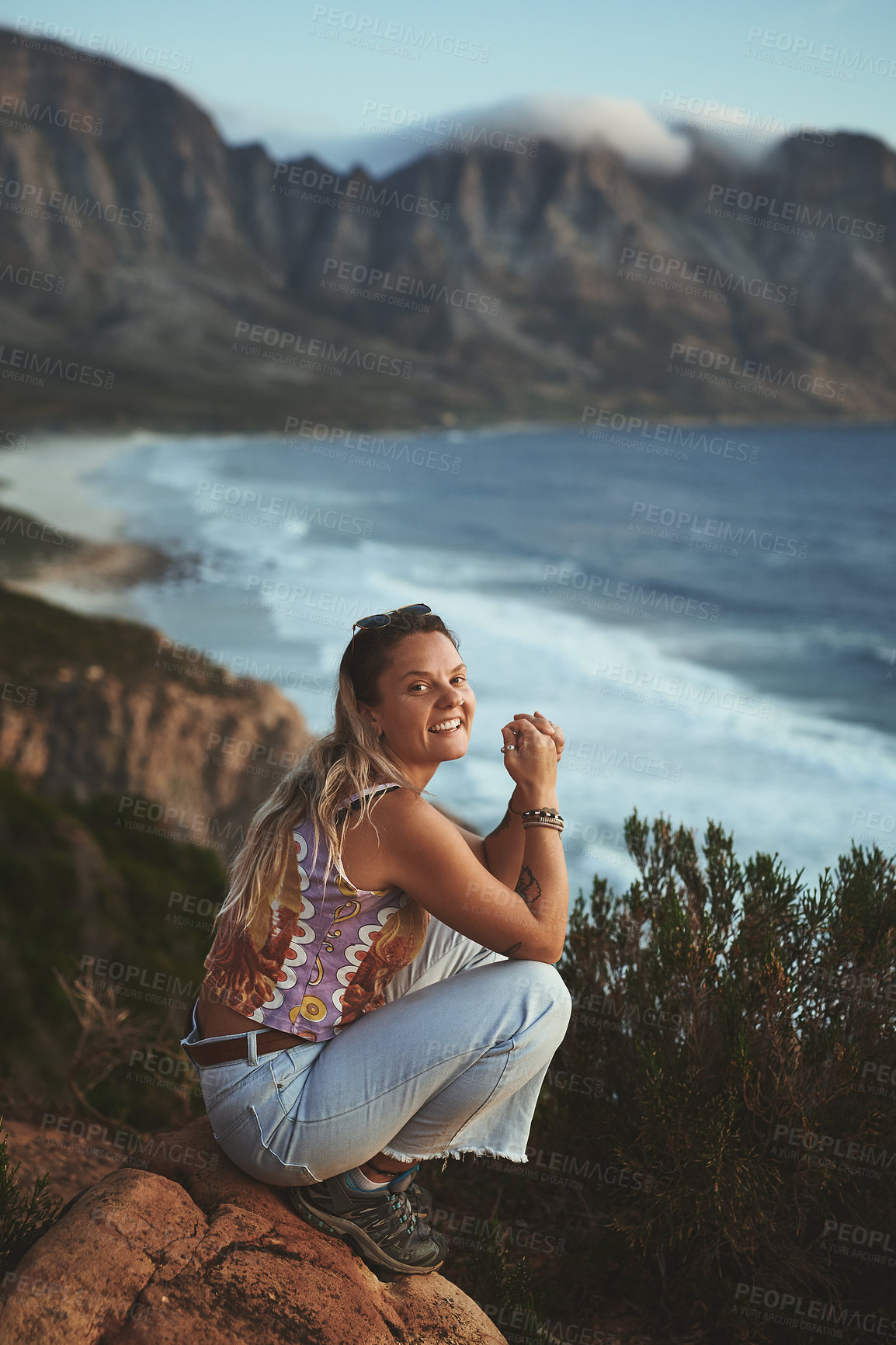 Buy stock photo Full length portrait of an attractive young woman crouched on the mountainside near the sea alone during a day outdoors