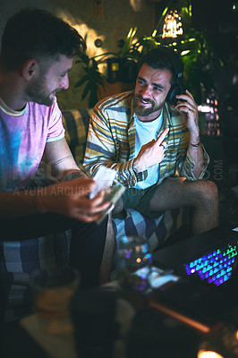 Buy stock photo Cropped shot of a handsome young man listening to music on a pair of headphones while sitting with his friend at home