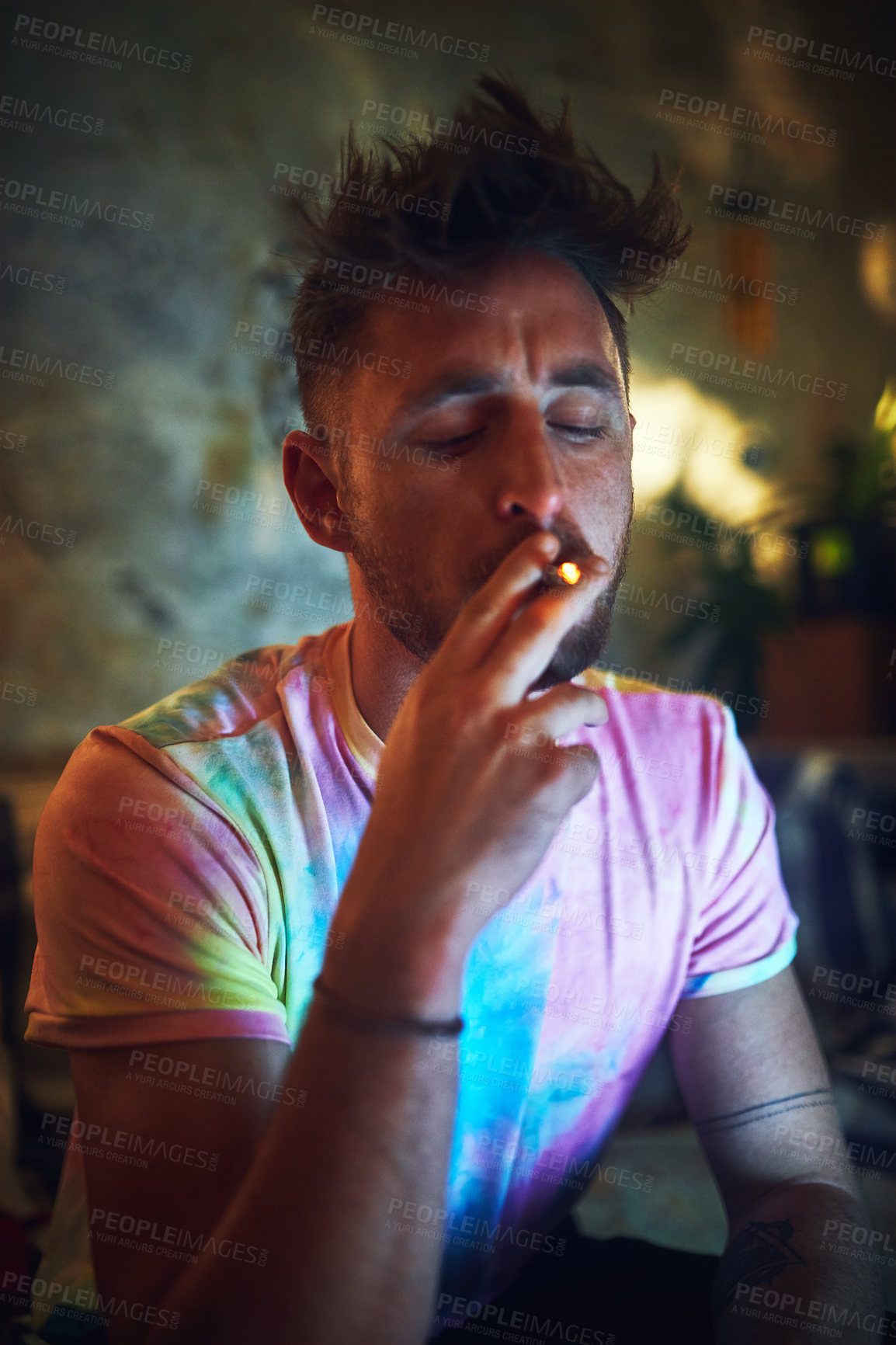Buy stock photo Cropped shot of a handsome young man smoking a blunt of cannabis while sitting alone at home