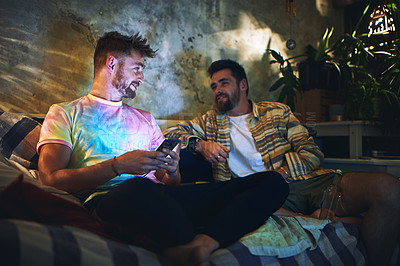 Buy stock photo Cropped shot of two handsome young men having a chat while hanging out together at home