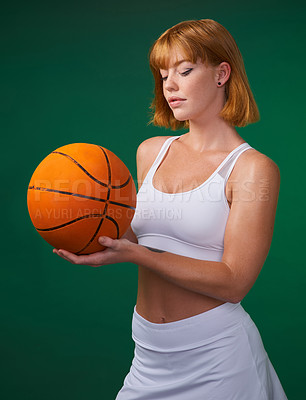 Buy stock photo Cropped shot of an attractive young sportswoman standing alone and holding a basketball against a green background in the studio