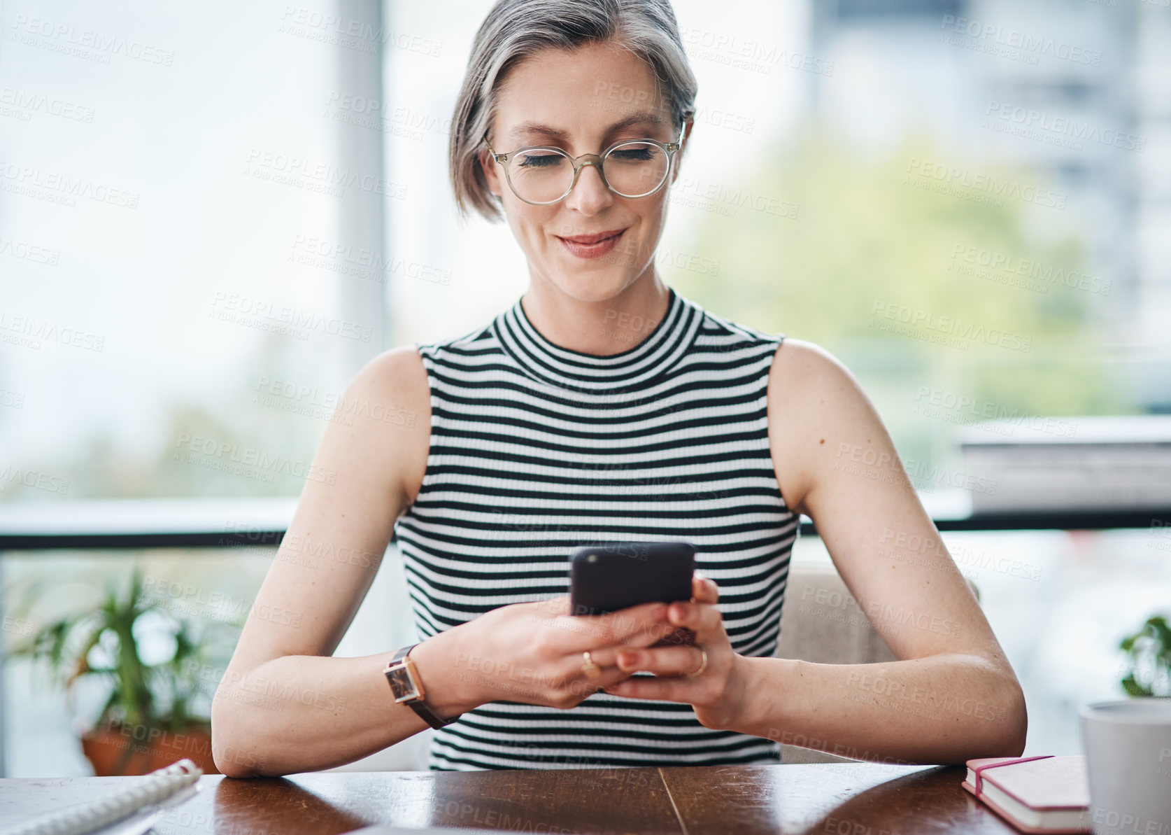 Buy stock photo Shot of a mature businesswoman using her cellphone while sitting at her desk