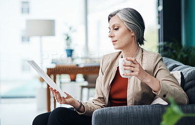Buy stock photo Cropped shot of an attractive mature businesswoman sitting alone and enjoying a cup of coffee while reading paperwork