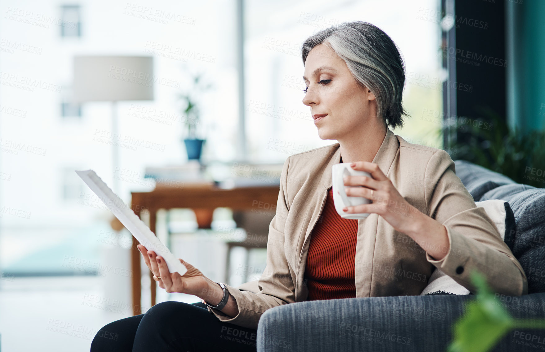 Buy stock photo Cropped shot of an attractive mature businesswoman sitting alone and enjoying a cup of coffee while reading paperwork