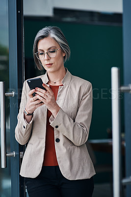 Buy stock photo Cropped shot of an attractive mature businesswoman standing alone and using her cellphone in her home office