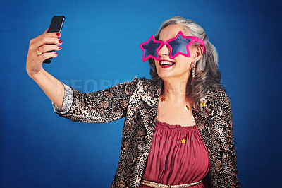 Buy stock photo Cropped hot of a funky and cheerful senior woman taking selfies against a blue background