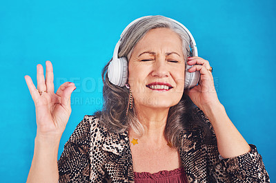Buy stock photo Cropped shot of a funky and cheerful senior woman listening to music on her headphones against a blue background