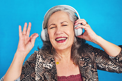 Buy stock photo Cropped shot of a funky and cheerful senior woman listening to music on her headphones against a blue background