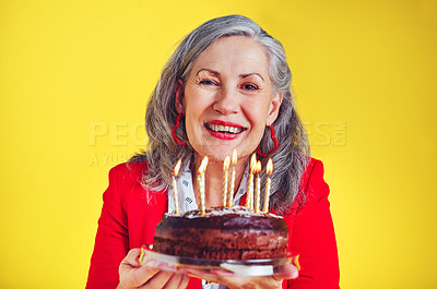 Buy stock photo Portrait of a cheerful senior woman holding a birthday cake against a yellow background