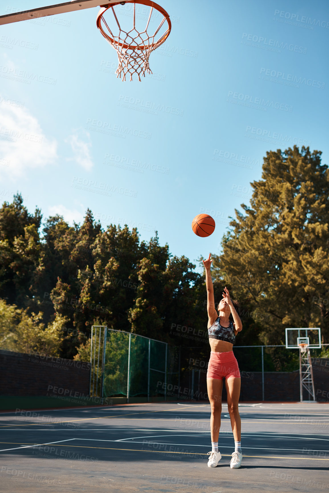 Buy stock photo Shot of a sporty young woman throwing a basketball into a net on a sports court