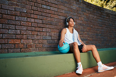 Buy stock photo Shot of a sporty young man taking a break after a game of basketball