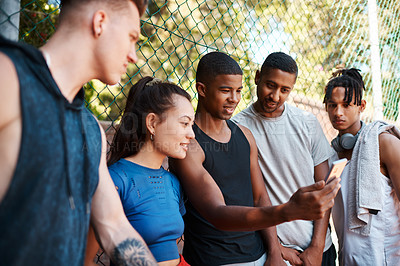 Buy stock photo Shot of a group of sporty young people looking at something on a cellphone while standing along a fence outdoors