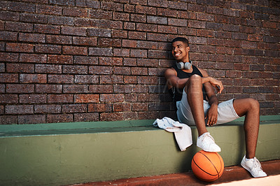 Buy stock photo Shot of a sporty young man taking a break after a game of basketball