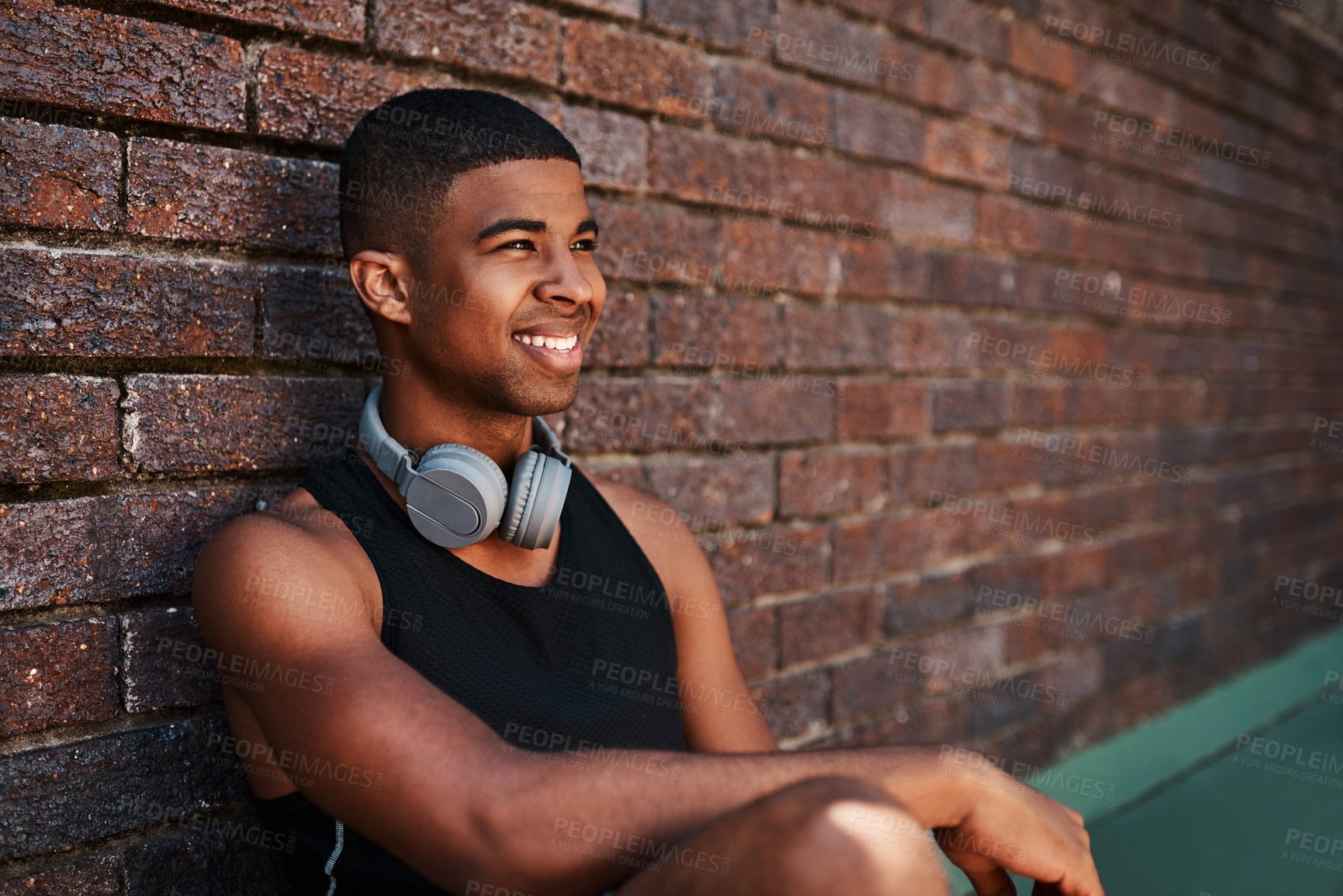Buy stock photo Shot of a sporty young man sitting against a wall outdoors