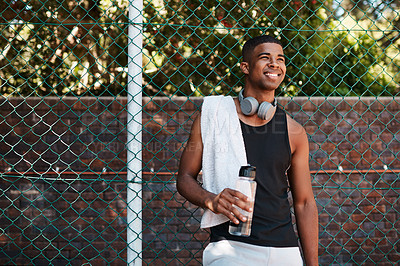 Buy stock photo Shot of a sporty young man taking a break while standing against a fence outdoors