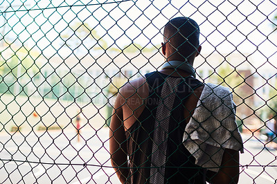 Buy stock photo Rearview shot of a sporty young man taking a break while standing against a fence on a sports court