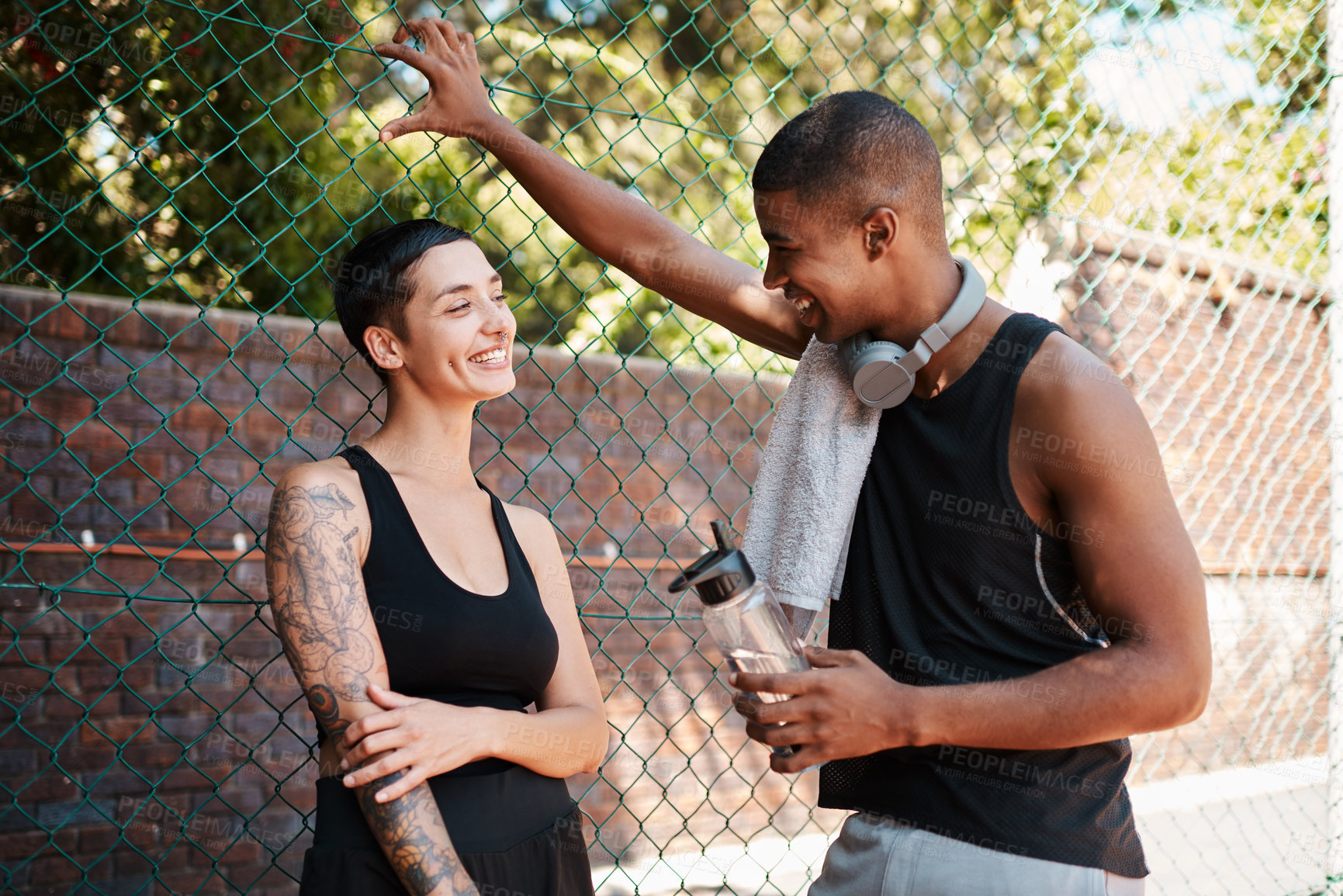Buy stock photo Shot of two sporty young people chatting to each other against a fence outdoors