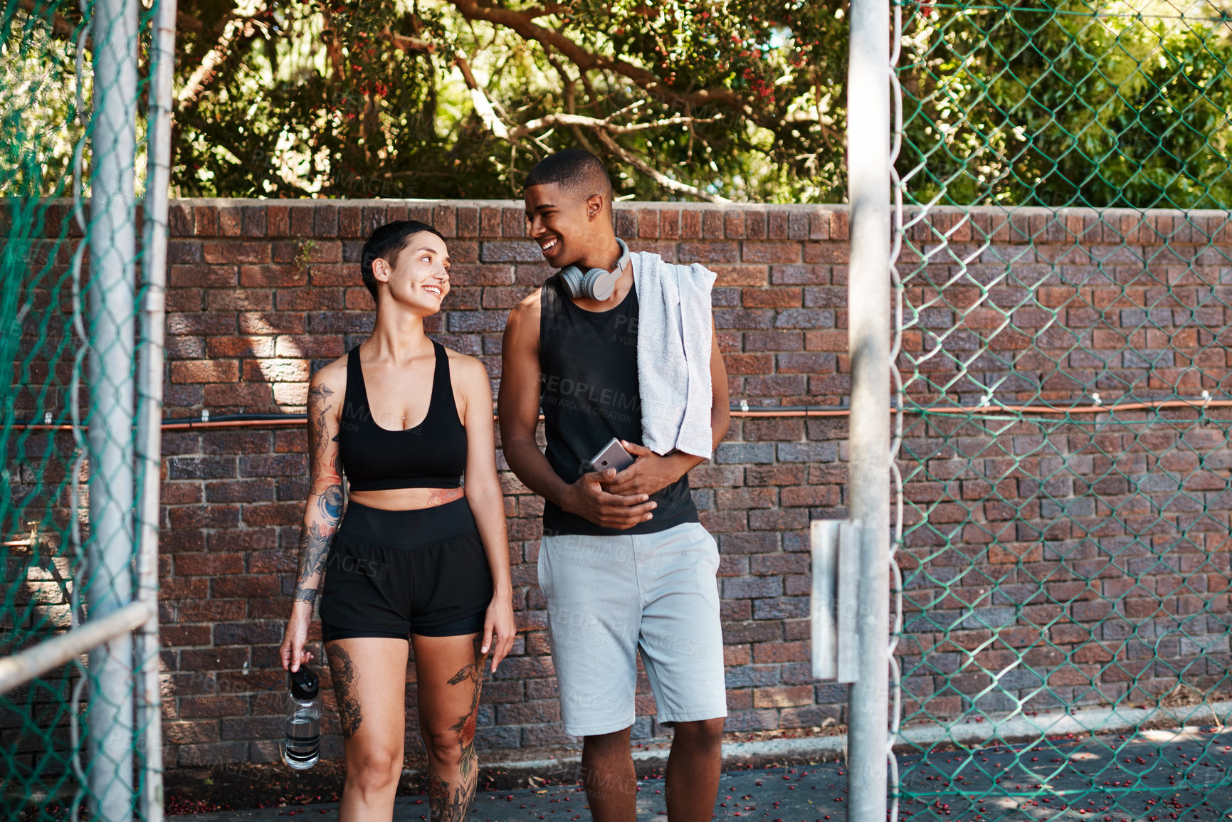 Buy stock photo Shot of two sporty young people chatting to each other while walking into a sports court