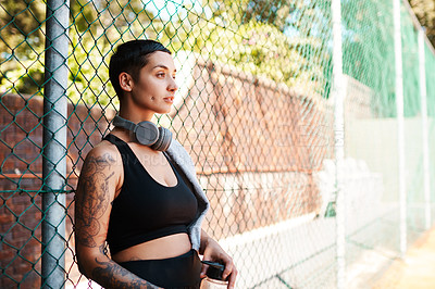 Buy stock photo Shot of a sporty young woman taking a break while standing against a fence outdoors