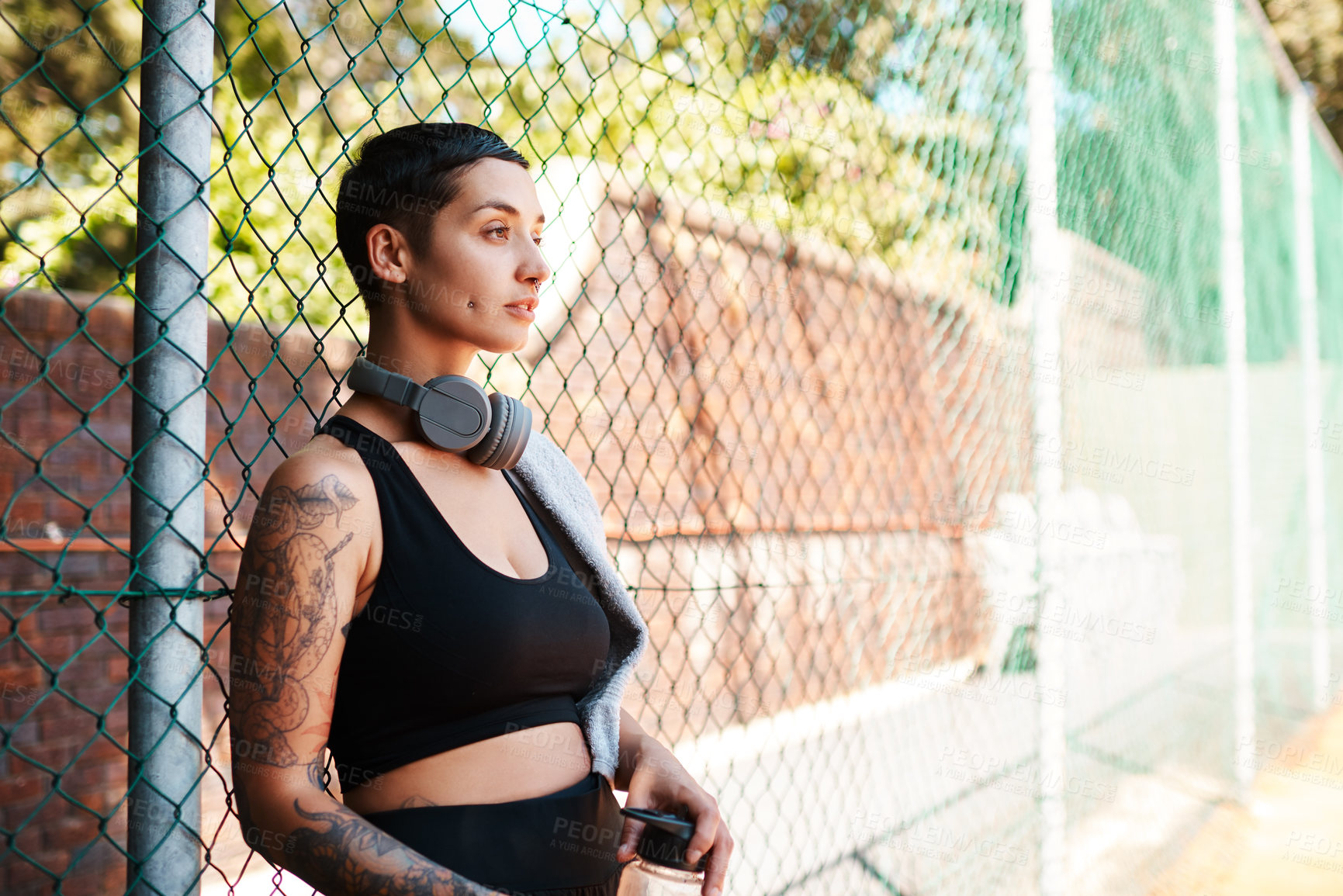 Buy stock photo Shot of a sporty young woman taking a break while standing against a fence outdoors