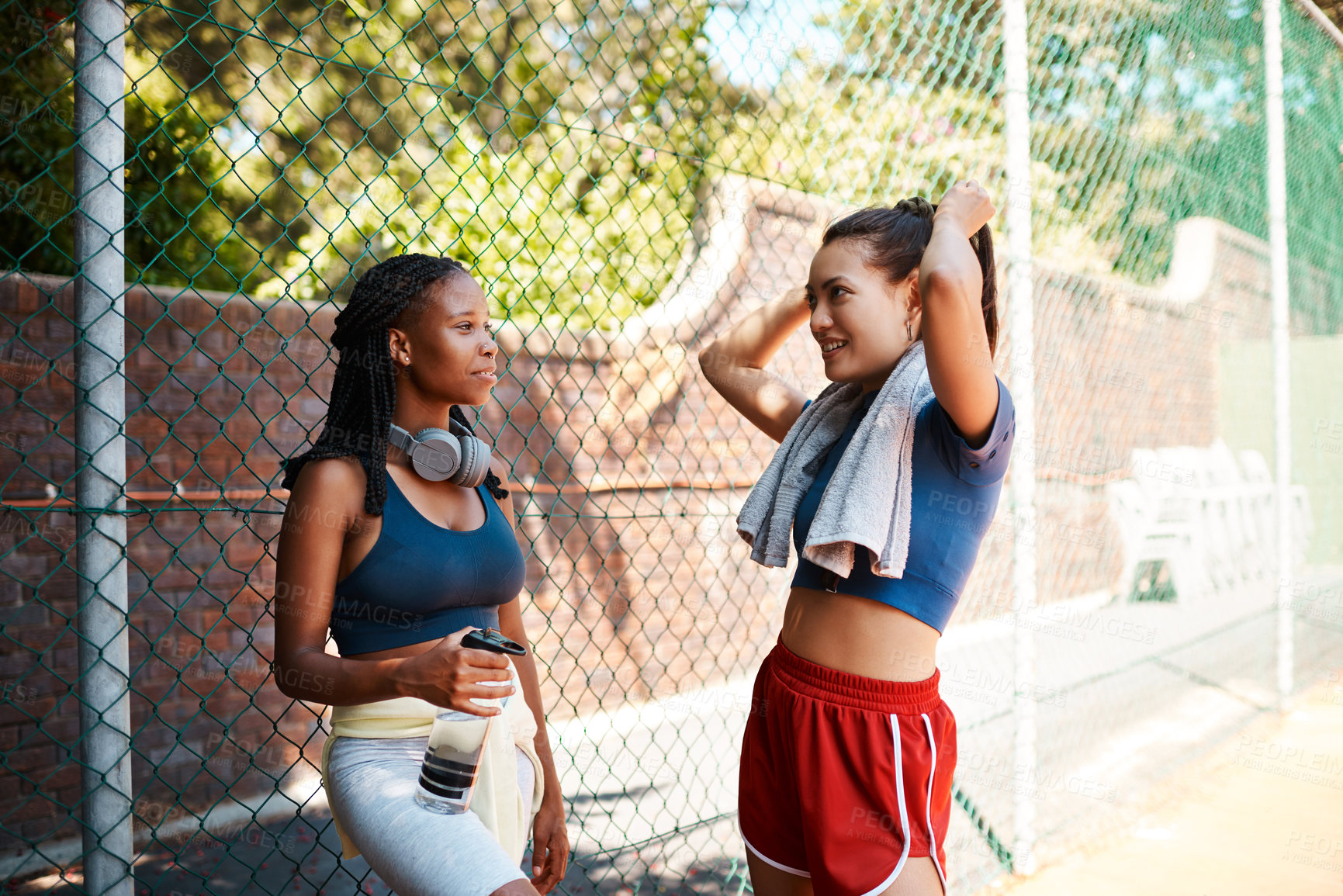 Buy stock photo Shot of two sporty young women chatting to each other against a fence outdoors