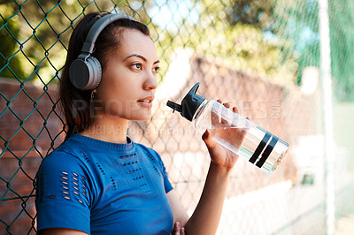 Buy stock photo Shot of a sporty young woman drinking water while standing against a fence outdoors