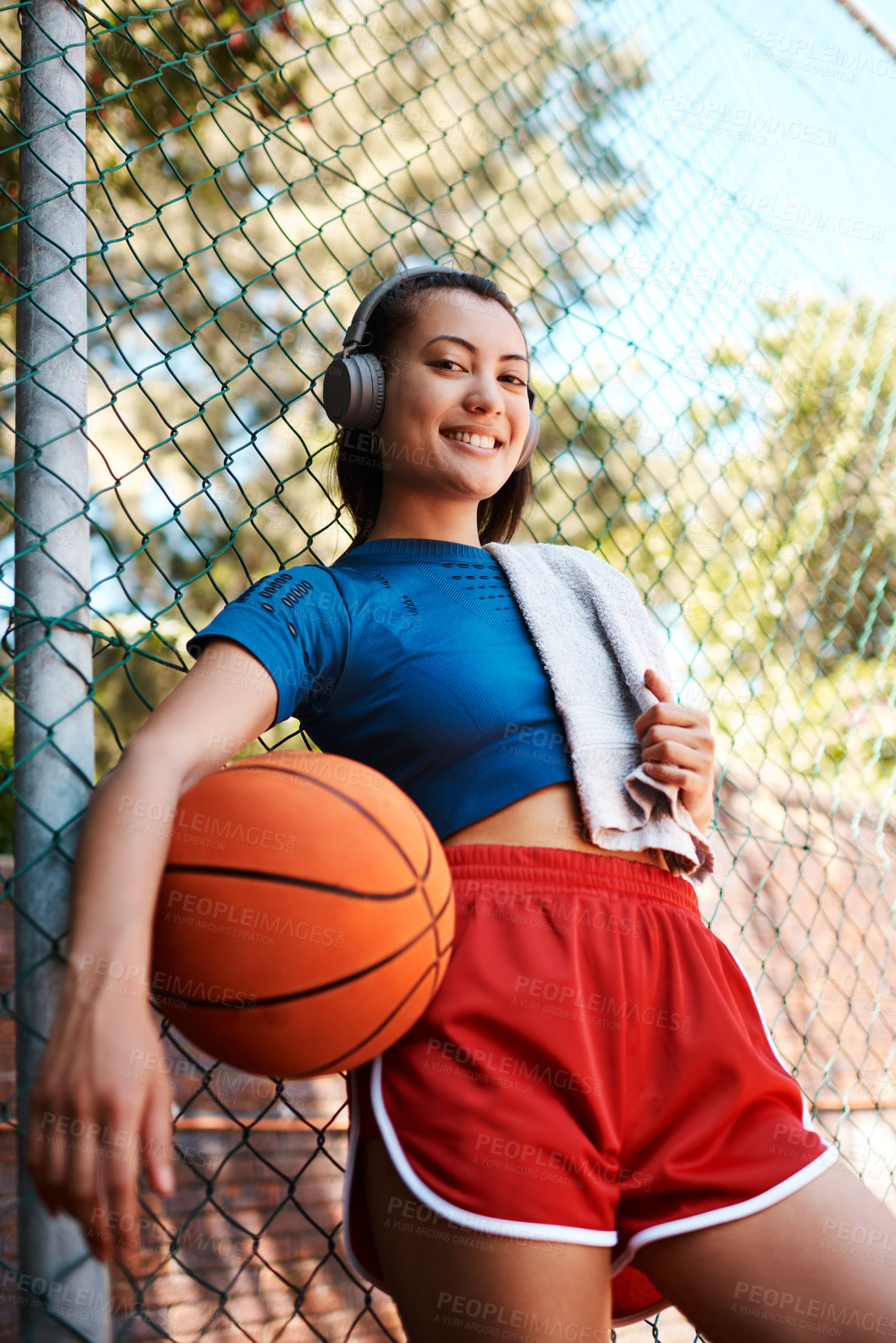 Buy stock photo Portrait of a sporty young woman holding a basketball while standing against a fence outdoors