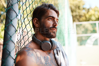 Buy stock photo Shot of a sporty young man taking a break while standing against a fence outdoors